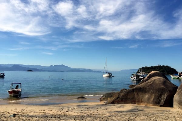 Une plage avec des bateaux, un voilier et des montagnes à l’horizon.