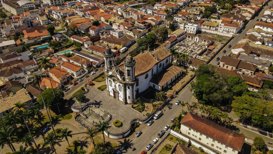 An aerial view of a historic town with a prominent church featuring a bell tower, surrounded by residential buildings and palm trees.
