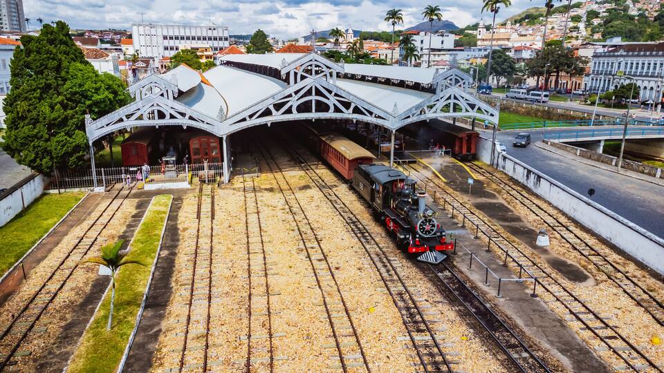 A vintage steam locomotive at a railway station with an arched roof and multiple tracks.