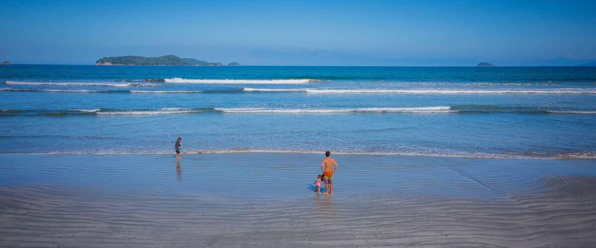 A beach with gentle waves, a clear sky, and distant islands.