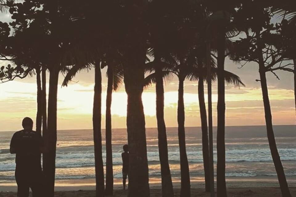 Een strand met palmbomen en de oceaan bij zonsondergang.