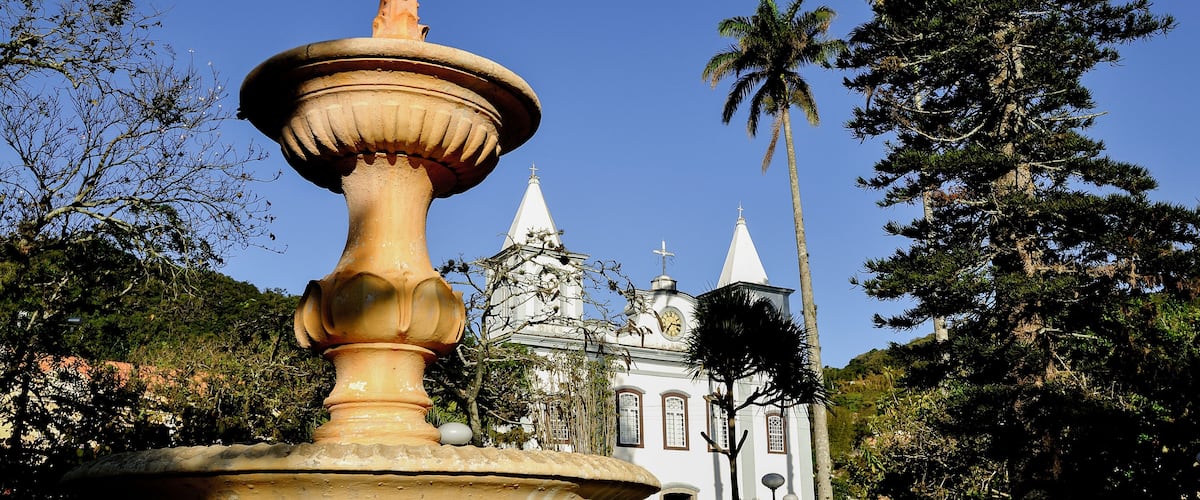 A large fountain, a church with a bell tower, and a palm tree in a park.