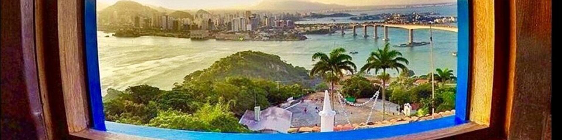 A panoramic view of a cityscape with a river, a bridge, and a hill with greenery.