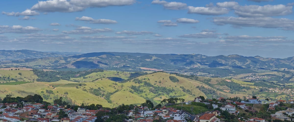 A town nestled in rolling hills with a backdrop of distant mountains under a partly cloudy sky.