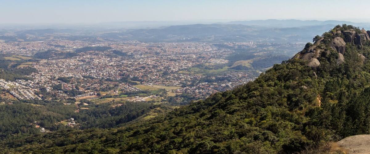 A mountainous landscape with a dense forest, a town in the valley, and a prominent rocky peak.