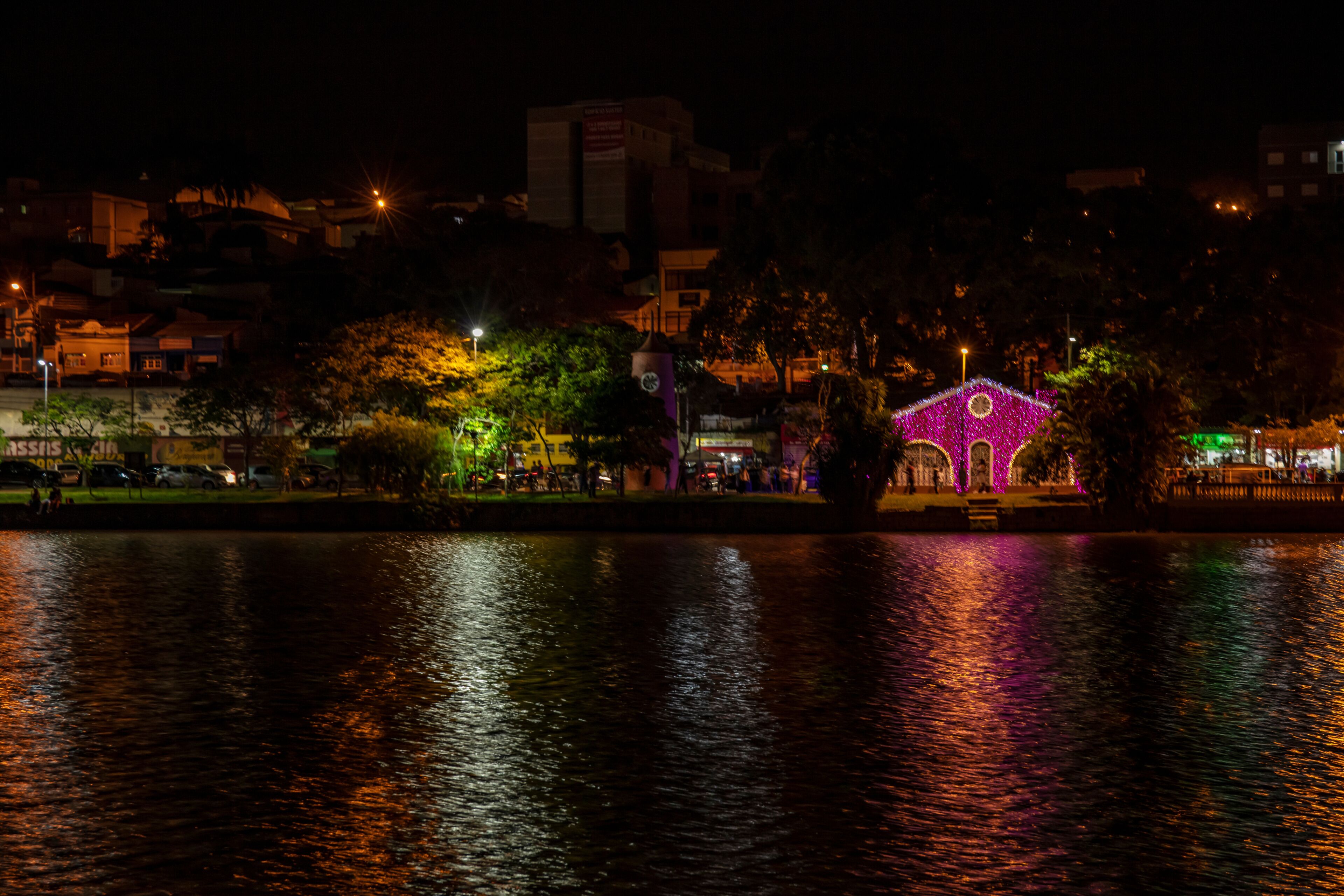 Vista nocturna de un río con un puente iluminado y edificios circundantes.