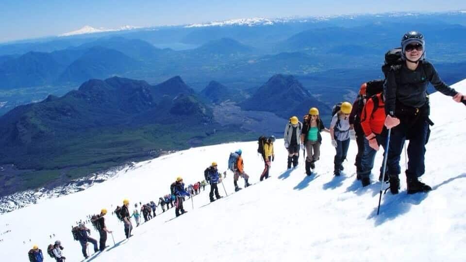 A group of hikers ascending a snowy mountain with a clear sky and distant snow-capped peaks.