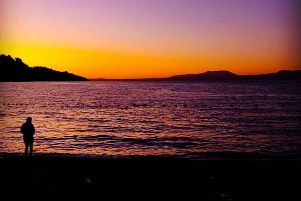 A silhouette of a person standing by a body of water during sunset.