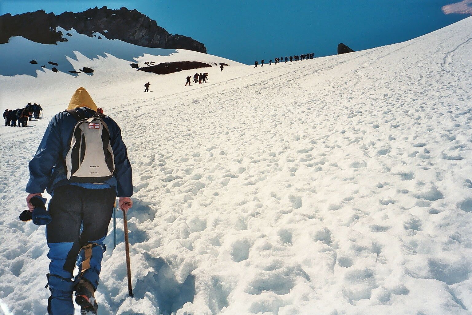 A snowy mountain landscape with a group of hikers ascending a slope.