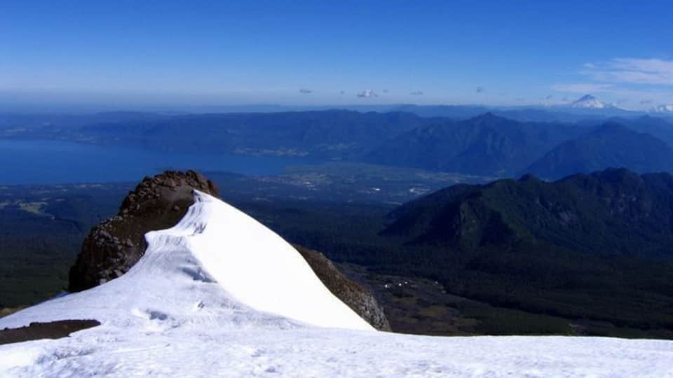 A snow-covered mountain peak with a clear view of distant mountains and a valley.