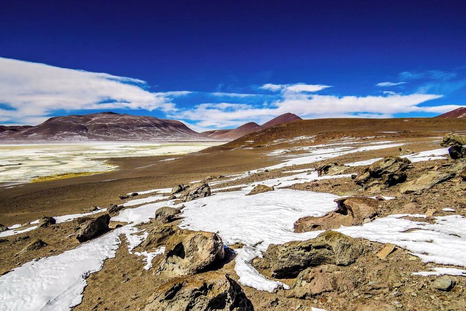 Eine gebirgige Landschaft mit Schneeflecken und felsigem Gelände unter blauem Himmel.