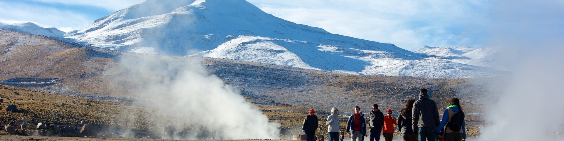 Campo de Géiseres El Tatio que incluye vista al desierto y montañas y también un pequeño grupo de personas