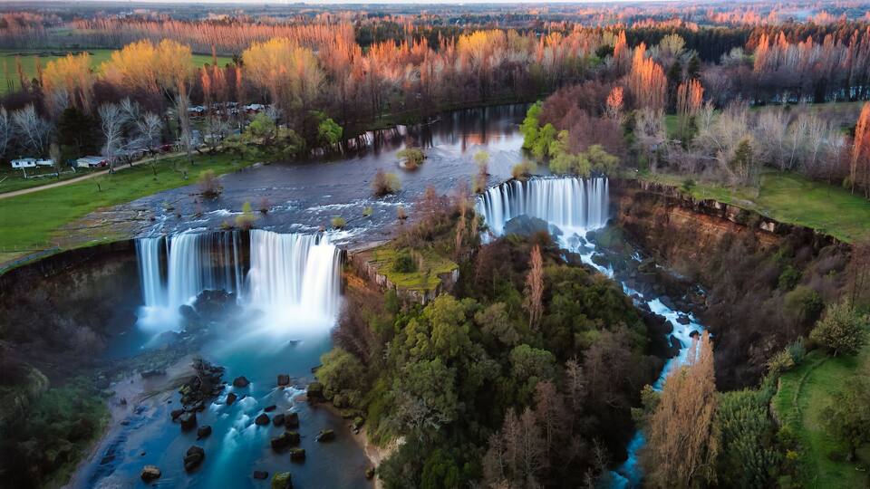 A waterfall cascading into a river surrounded by autumn-colored trees.