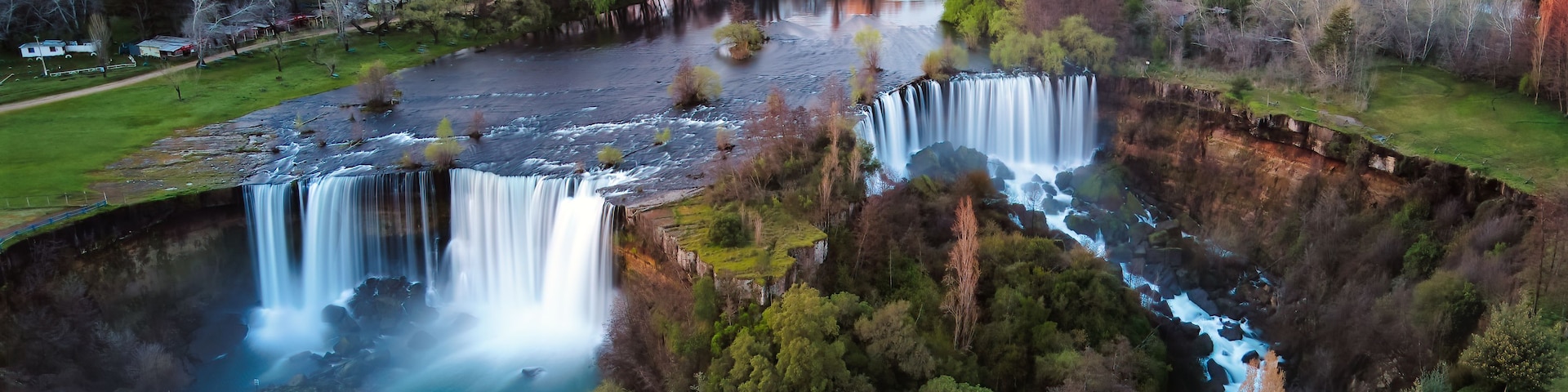 A waterfall cascading into a river surrounded by autumn-colored trees.