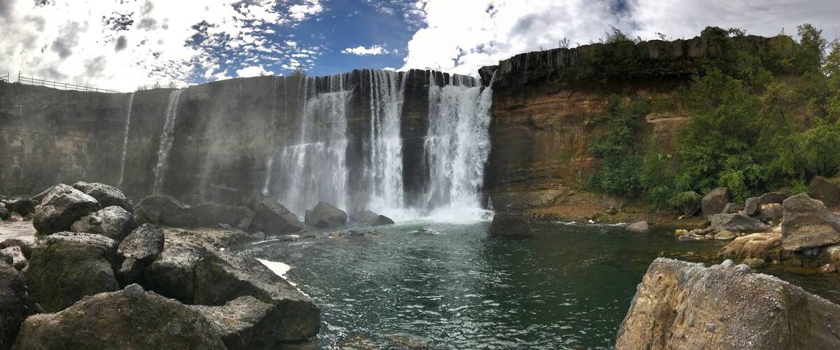 A waterfall cascading over a cliff into a river surrounded by rocks and greenery.