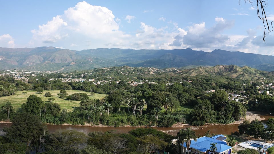 A river flowing through a valley with a town and mountains in the background.