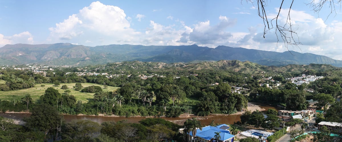 A river flowing through a valley with a town and mountains in the background.