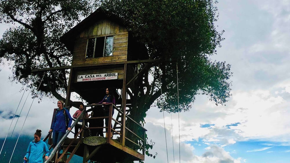 Et træhus kaldet "La Casa del Arbol" med et skilt, der angiver, at det ligger i Baños, Ecuador.