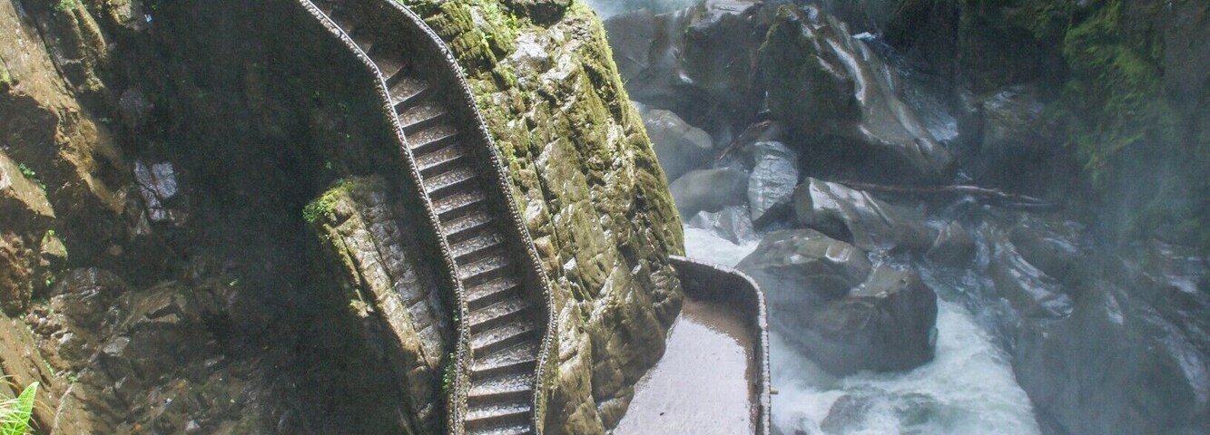 Uma escadaria de pedra serpenteia por um penhasco íngreme, descendo até um rio lá embaixo.