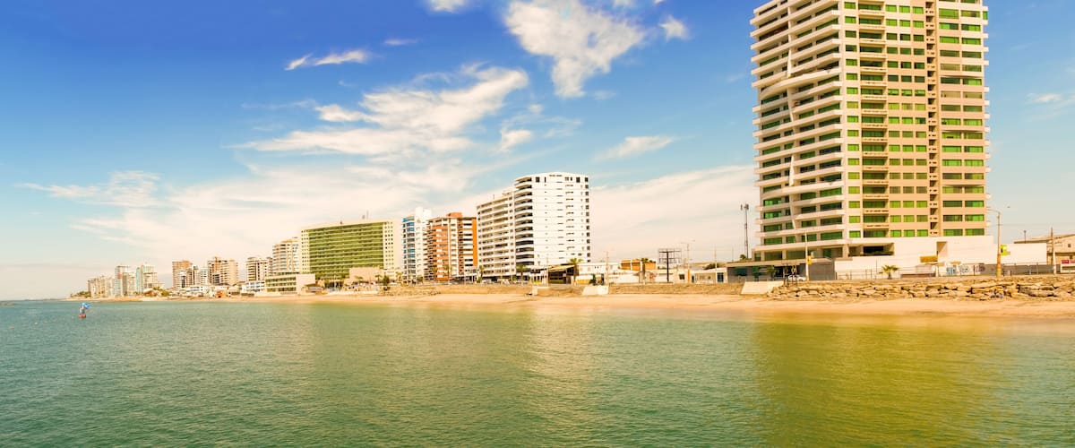 A coastal cityscape with high-rise buildings, a sandy beach, and calm sea.