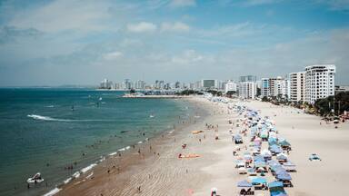 A beach with people, umbrellas, and buildings in the background.