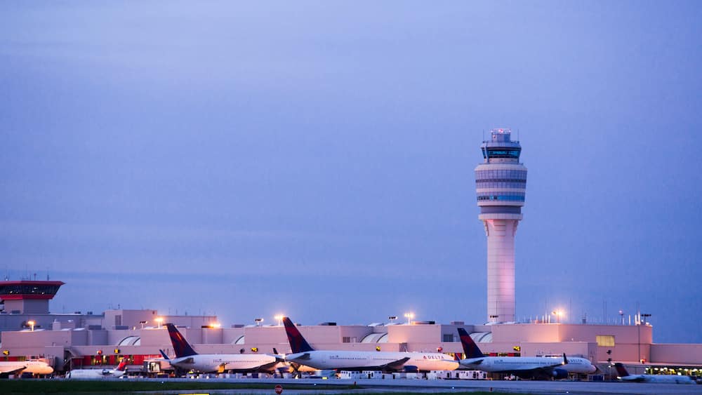 An airport with multiple airplanes parked, a control tower, and terminal buildings.