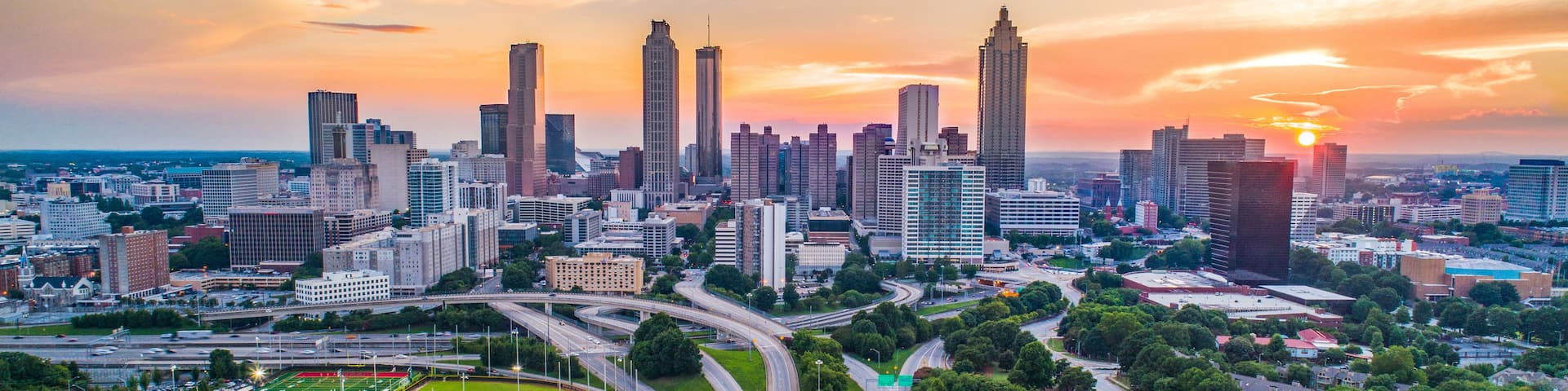 A city skyline with high-rise buildings, a highway, and residential areas during sunset.