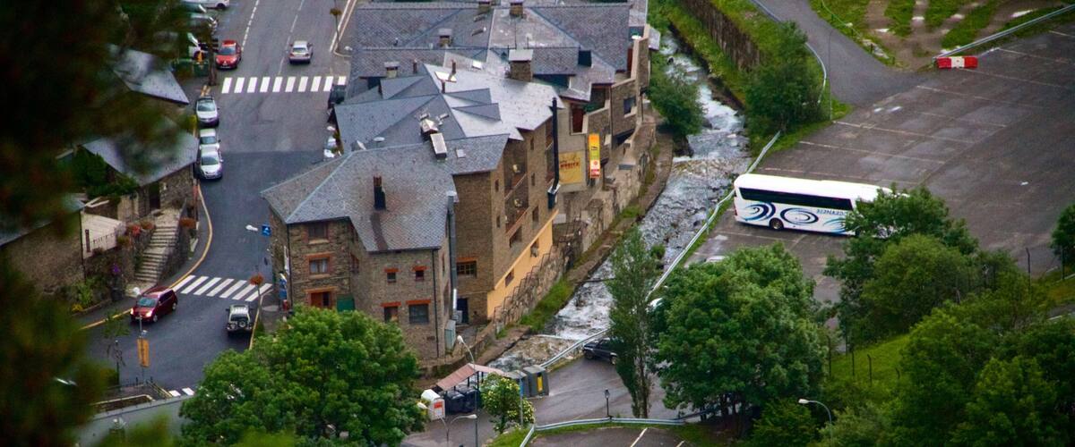 A historic stone building with a steep roof, a bus stop, and a parking lot.