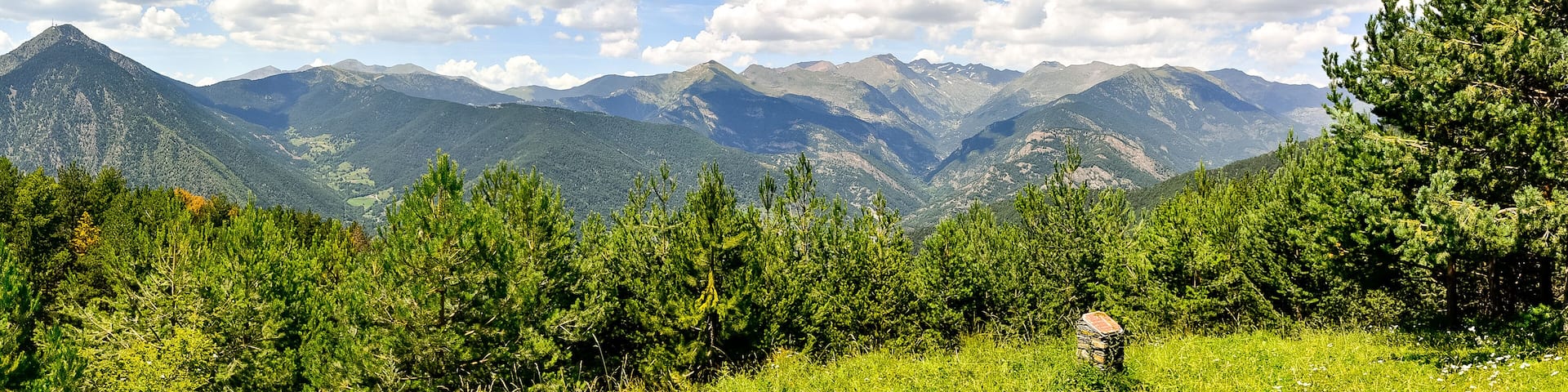 A mountainous landscape with dense green forests and a clear blue sky with scattered clouds.