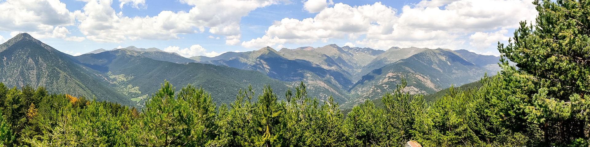 Un paisaje montañoso con bosques verdes y frondosos, y un cielo azul despejado con algunas nubes.