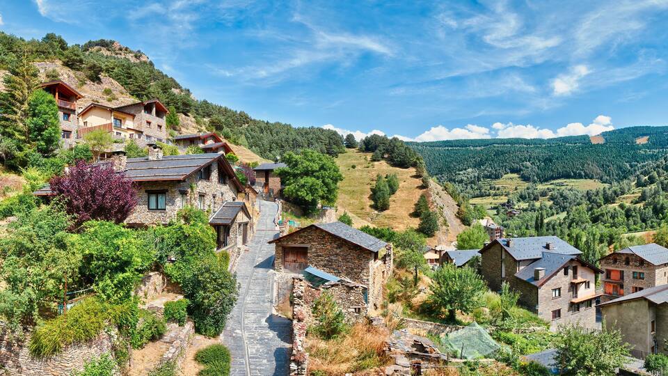 A hillside village with stone houses, a winding road, and a mountainous backdrop.