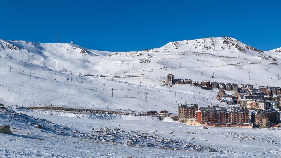 A snow-covered mountain with a ski resort and buildings.