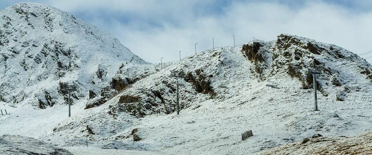 A snowy mountain landscape with sparse vegetation and a clear sky.