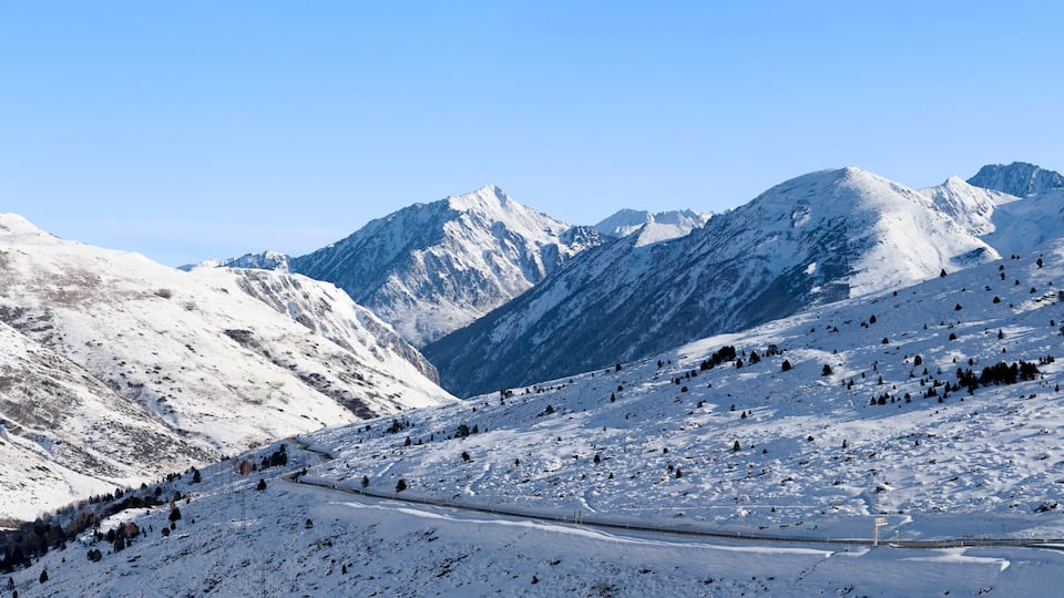 A snow-covered mountain landscape with a winding road and a clear blue sky.