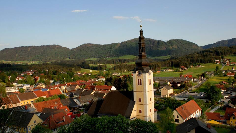 A town with a prominent church tower, surrounded by houses and rolling hills.