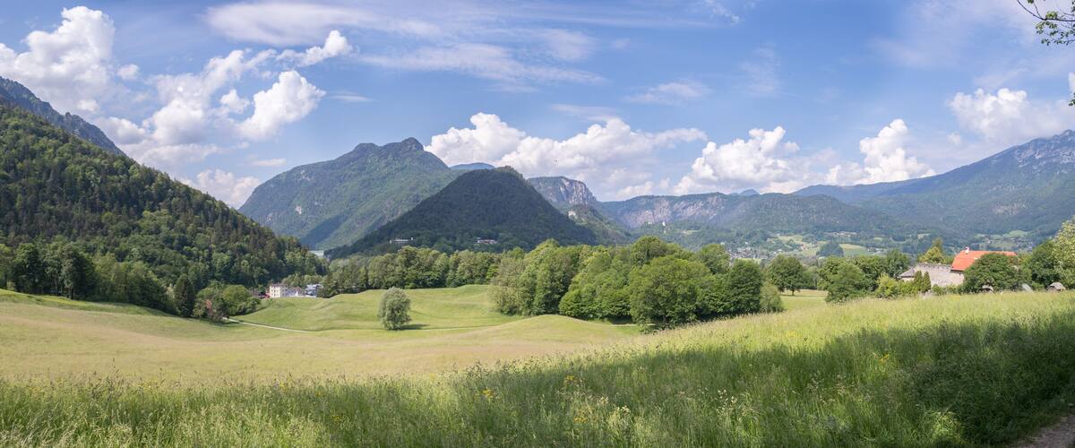 A lush green valley with rolling hills, a prominent mountain peak, and scattered houses.