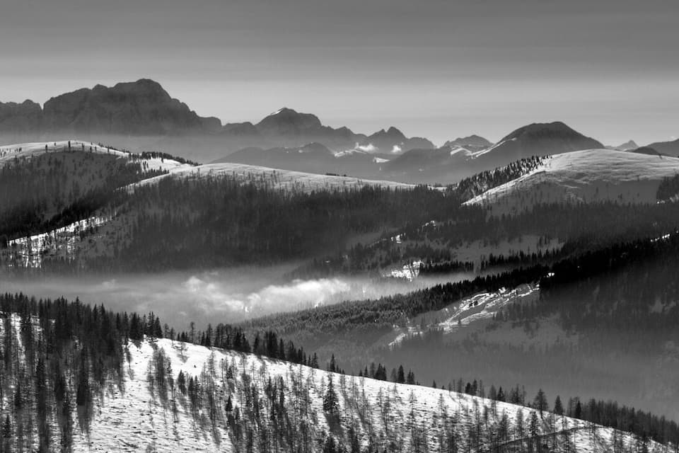 Eine gebirgige Landschaft mit schneebedeckten Hängen und dichten Wäldern.