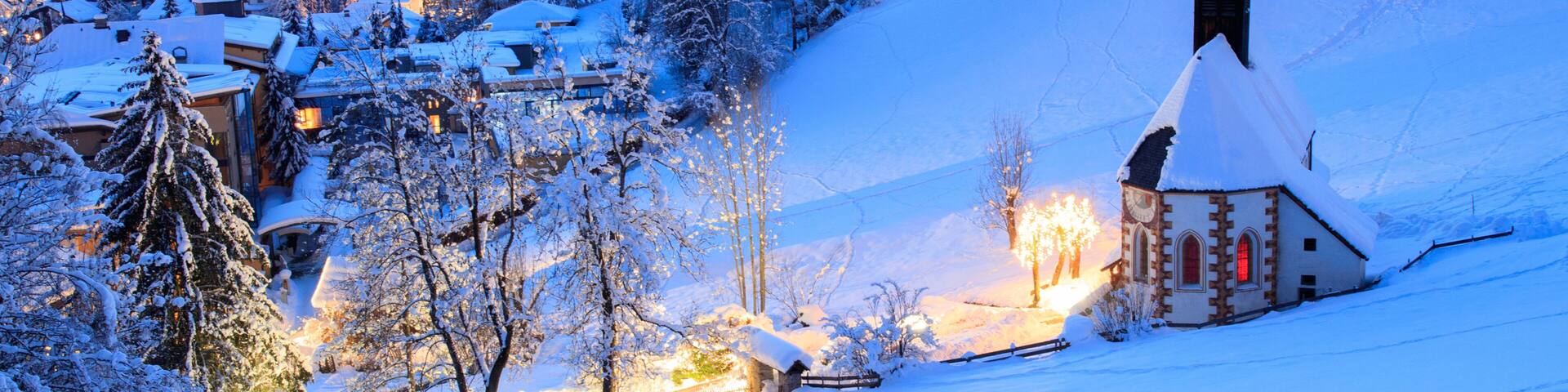 A snow-covered village with a church, houses, and a mountain backdrop.