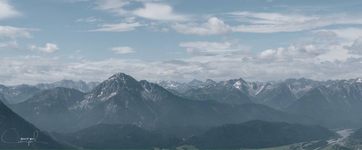 A mountain range with snow-capped peaks under a partly cloudy sky.