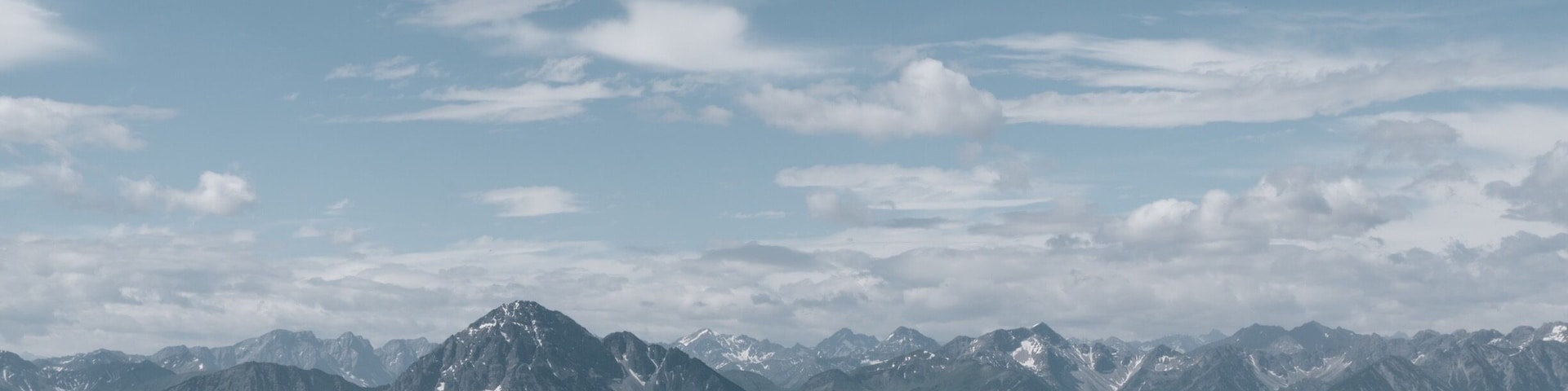 A mountain range with snow-capped peaks under a partly cloudy sky.