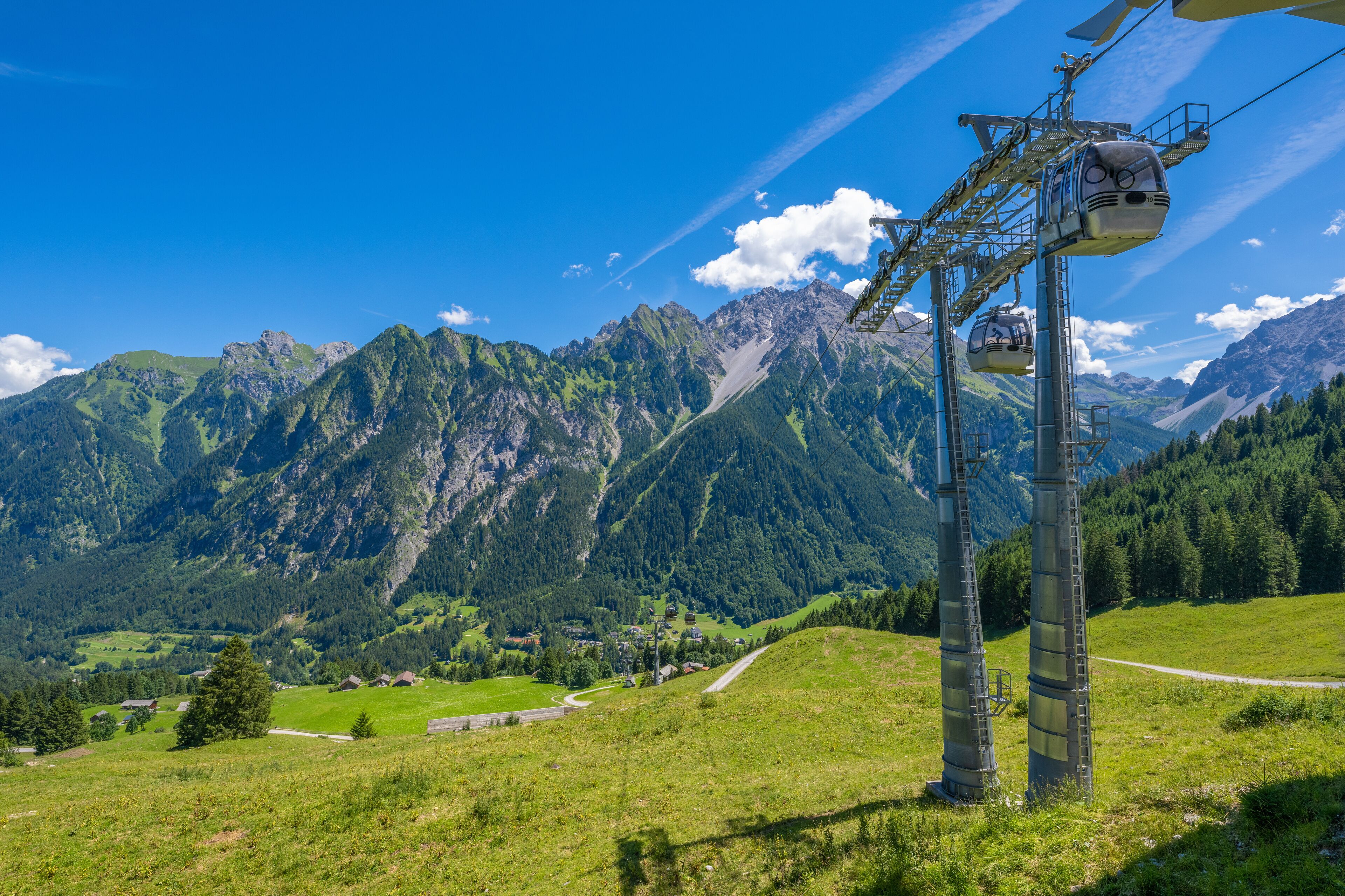 A cable car system in a mountainous area with green valleys and rocky peaks.