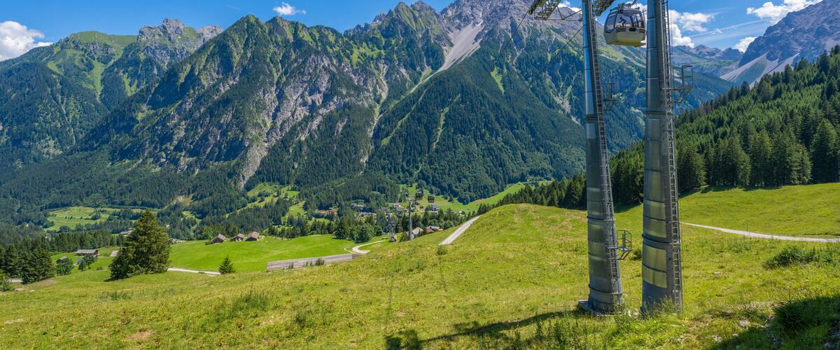 A cable car system in a mountainous area with green valleys and rocky peaks.