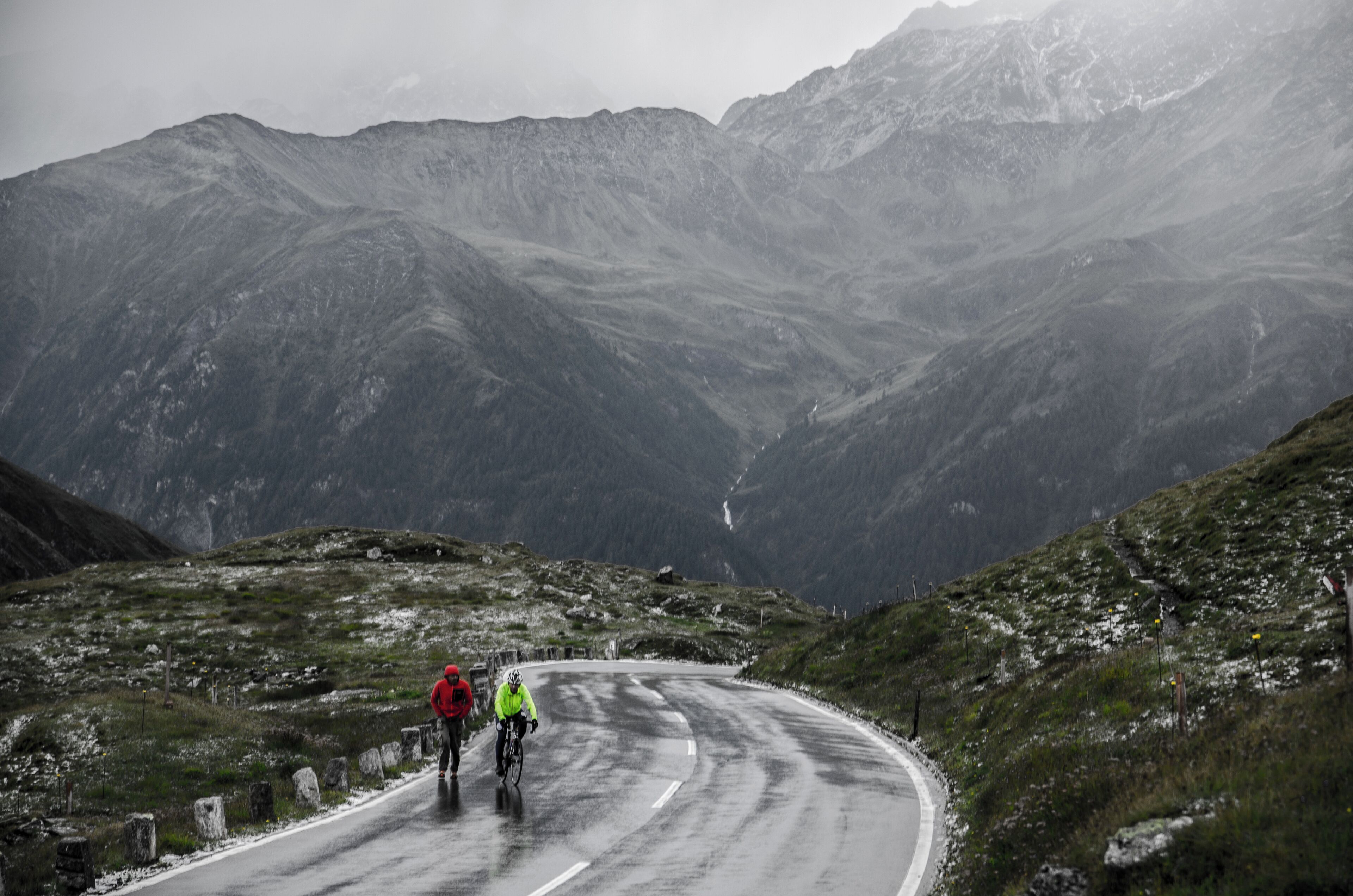 A winding road through a mountainous landscape with two cyclists.