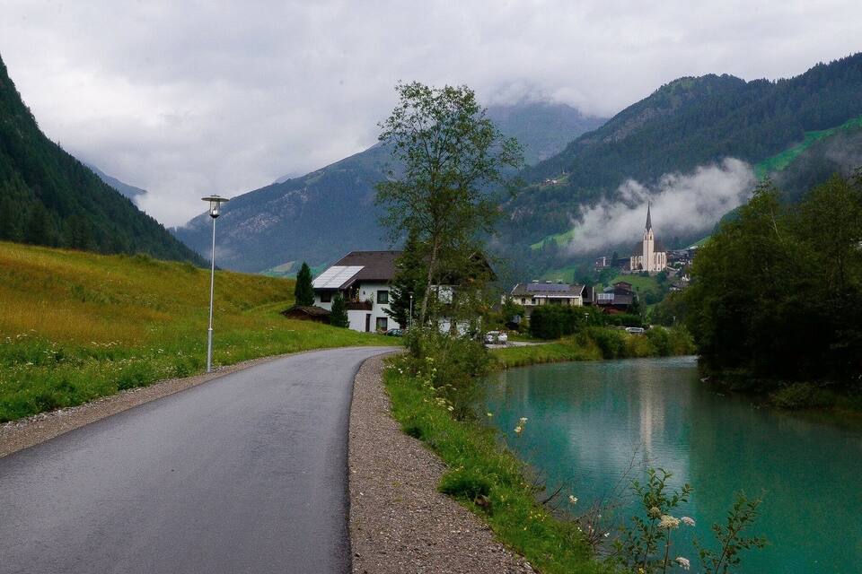 En slingrande väg längs en stilla sjö, omgiven av frodig grönska och berg.