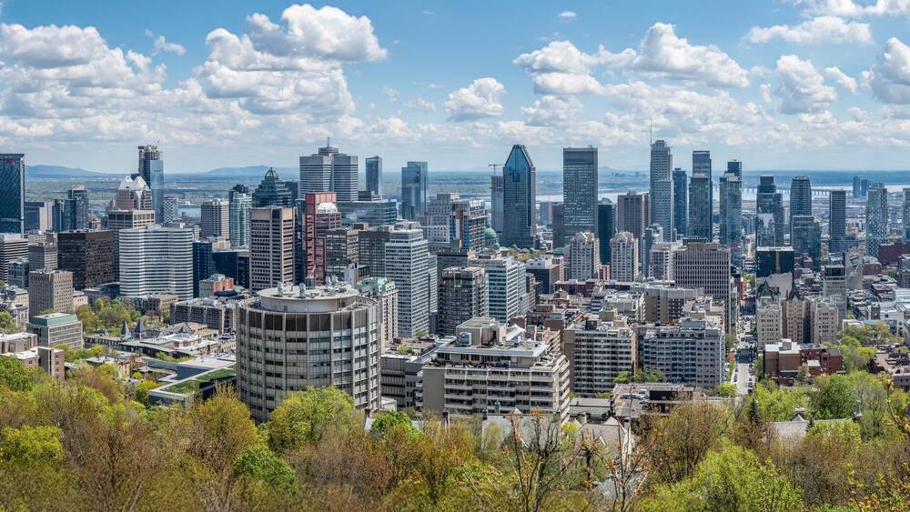 Un paysage urbain dense, avec de modernes gratte-ciel, une rivière en arrière-plan et un pont enjambant la rivière.