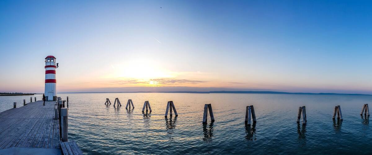 A lighthouse and wooden posts on a pier at sunset.
