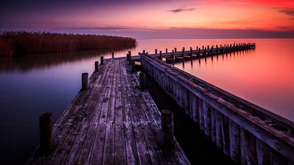 A wooden pier extending into calm water with a sunset sky.