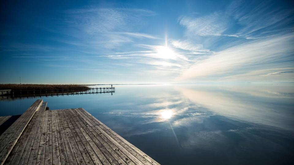 A wooden pier extending into calm waters with a clear sky and distant horizon.