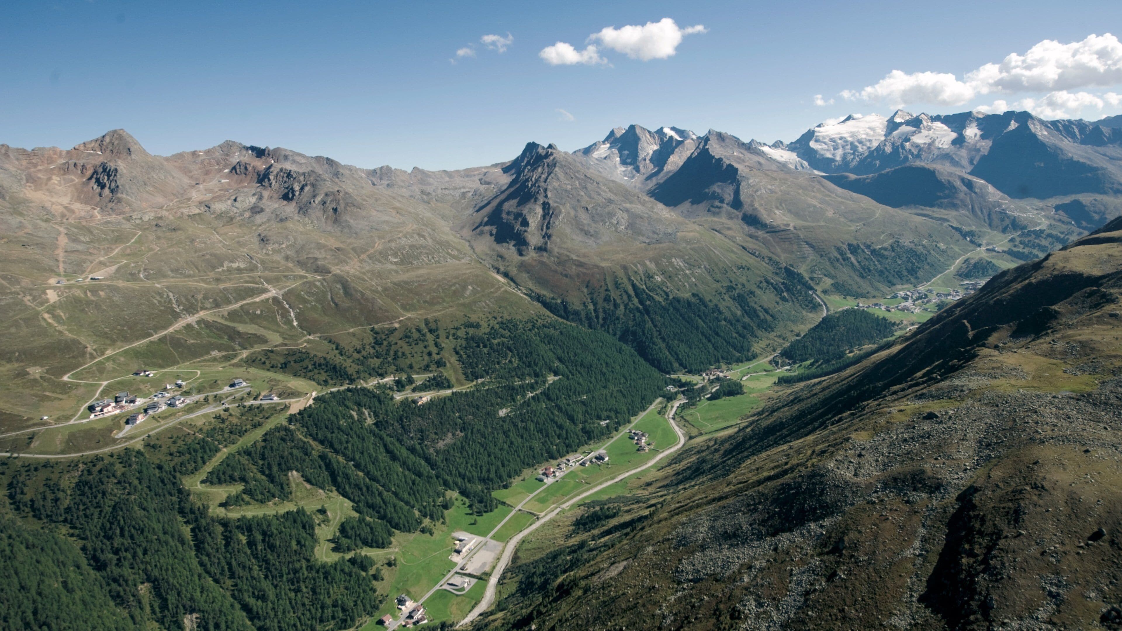 A mountainous landscape with a valley, forested areas, and a small settlement.