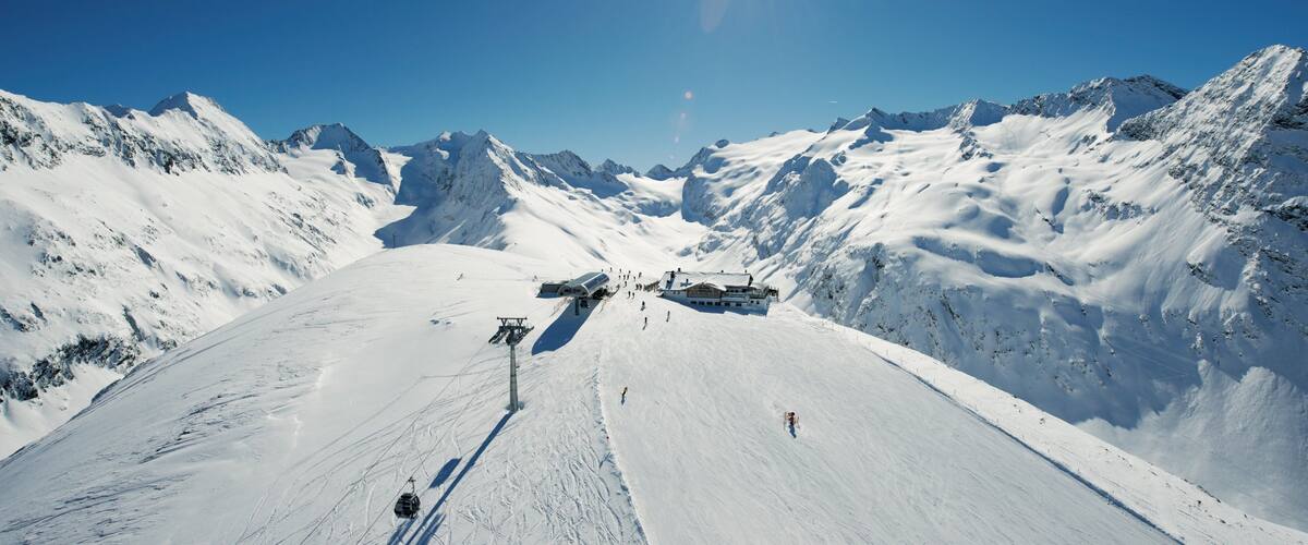 A snowy mountain slope with a ski lift, a lodge, and a clear blue sky.